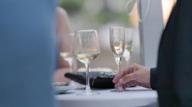 Misafirler soğuk beyaz şarap bardakları tutuyor ve zarif bir açık hava resepsiyonunda taze istiridye yiyorlar.