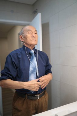İşitme cihazı olan yaşlı bir işadamı modern bir banyoda hazırlanırken kıyafetlerini düzeltiyor.