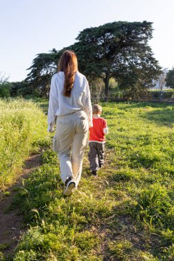 Anne ve oğlu güneşli bir günde canlı yeşil bir çayırda keyifli bir gezinti yapıyorlar.