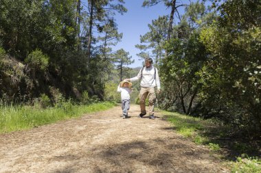 Baba ve oğul yemyeşil yemyeşil ile çevrili güneşli bir orman yolunda sakin bir yürüyüş yapıyorlar.