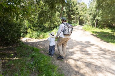 Baba ve oğul, güneşli bir yaz gününde doğa yürüyüşü yaparak orman yolunu keşfediyorlar.