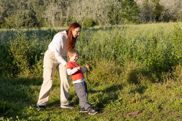 Mutlu anne ve oğul güneşli bir günde tarlada eğleniyor, yabani bitkilerle oynuyor.