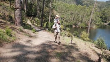 Babam göl kenarında yürürken çocuğu omuzlarında taşır.