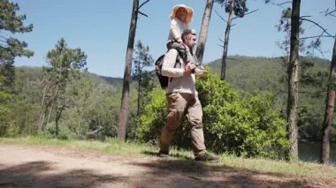 Mutlu baba doğada yürürken küçük oğlunu omuzlarında taşıyor.