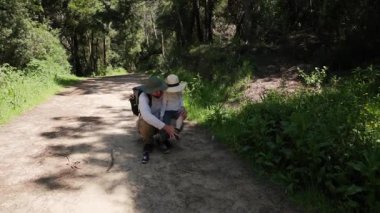 Sorumlu baba, güneşli bir yürüyüş yolunda mola verirken küçük çocuğuna ayakkabılarını bağlamasında yardım ediyor.
