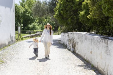 Anne ve oğlu güneşli bir kırsalda sakin bir yürüyüşün keyfini çıkarıyorlar.