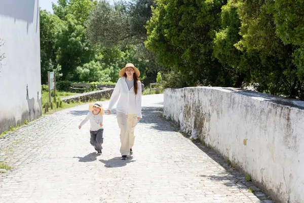 Anne ve oğlu güneşli bir kırsalda sakin bir yürüyüşün keyfini çıkarıyorlar.