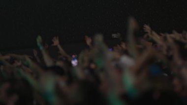 İzleyiciler bir gece konserinde el kaldırıyor, canlı müzikten zevk alıyorlar.