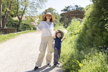 Anne ve oğul şapka takıyor ve gülümsüyor. Kır yolunda güneşli bir günün tadını çıkarıyorlar.