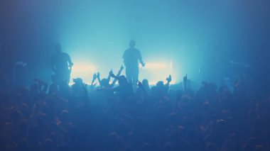 Canlı, dumanlı bir konser salonunda çalan müzisyenlerin silueti coşkulu hayranlarla meşgul oluyor.