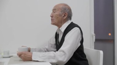 Masada oturan kıdemli adam, kahve ve bisküvilerin tadını çıkarıyor.