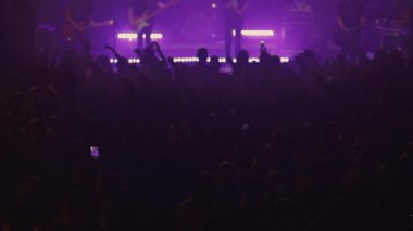 Enerjik kalabalık mor sahne ışıkları altında canlı müzik performansını seviyor