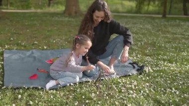 Anne ve kızı birlikte güzel vakit geçiriyorlar. Parkta dallarla küçük bir yapı inşa ediyorlar.