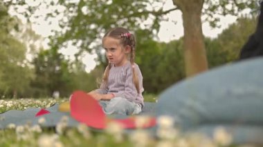 Parkta pervane oynayan genç bir kız ailesiyle battaniyenin üzerinde oturuyor.