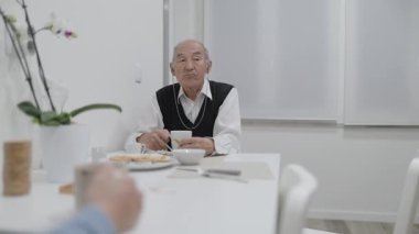 Evde kahvaltıda işitme cihazlı kıdemli adam konuşuyor.