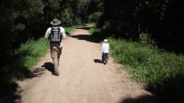 Baba ve oğul yemyeşil yemyeşil bir yolda sakin bir yürüyüşün tadını çıkarıyorlar.