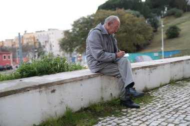 Yaşlı bir adam, şehir parkındaki alçak bir duvarda oturmuş, huzurlu atmosferin tadını çıkarırken bir not defterine not alıyor.
