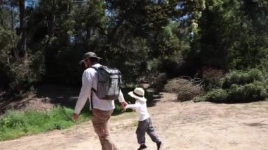 Baba ve oğul güneşli bir doğa yolunda keyifli bir yürüyüş yapıyorlar.