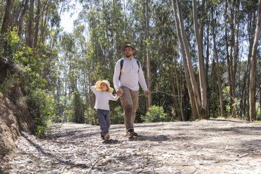 Baba ve kızı güneşli bir okaliptüs ormanında yürüyüp aile bağlarını ve açık hava maceralarını destekliyor.
