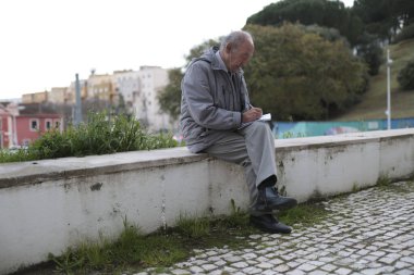 Şehir parkında alçak duvarda otururken kıdemli gazeteci notlar alıyor.