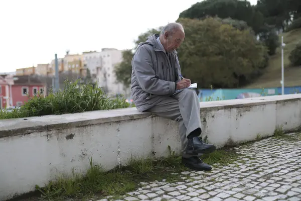 Şehir parkında alçak duvarda otururken kıdemli gazeteci notlar alıyor.