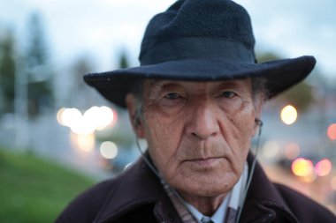 Şapka takan ve şehir merkezinde kulaklıkla müzik dinleyen ciddi bir son sınıf öğrencisinin yakın çekimi.