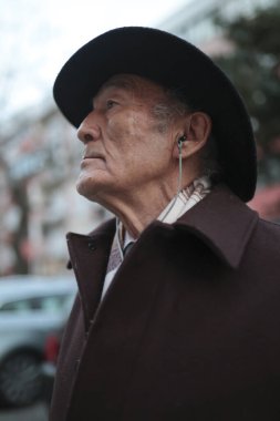 Şık bir son sınıf öğrencisi, şehir caddesinde yürürken, şapka ve palto giyerken müzik dinliyor.