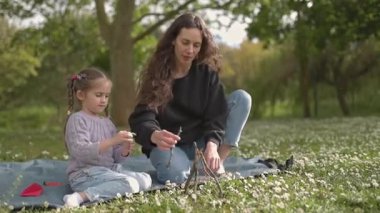 Anne ve kızı birlikte güzel vakit geçiriyorlar. Huzurlu bir park ortamında dallarla küçük bir yapı inşa ediyorlar.