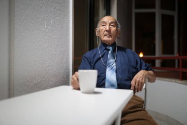 Yaşlı profesör müzik dinliyor ve geceleri balkonunda kahve içiyor.