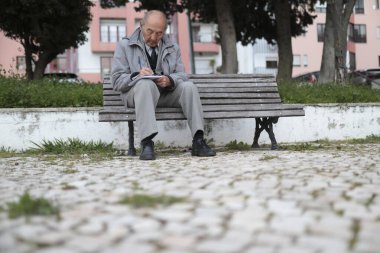 Yaşlı profesör park bankında otururken not defterine not alıyor.