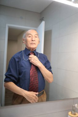 Kıdemli işadamı sabah banyodaki aynanın önünde kravatını düzeltiyor.