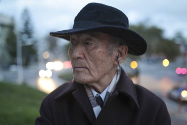 Şık bir kıdemli adam şapka ve kulaklık takıyor, alacakaranlıkta şehrin atmosferinin tadını çıkarıyor.