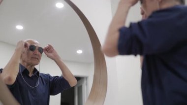 Yaşlı adam dans ediyor ve aynanın önünde güneş gözlüğü takıyor.