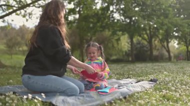 Anne ve kızı güneşli bir parkta renkli kağıt kalplerle oynayarak birlikte kaliteli vakit geçirmekten zevk alıyorlar.