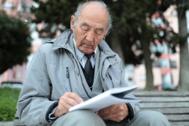 Kıdemli profesör bankta müzik dinlerken notlar alıyor.