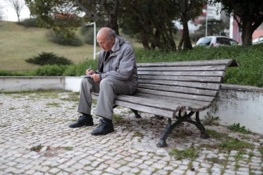 Huzurlu bir parktaki ahşap bir bankta otururken not alan yaşlı bir adam.