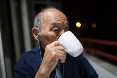 Yaşlı işadamı geceleri balkonunda sıcak bir içecek içiyor.