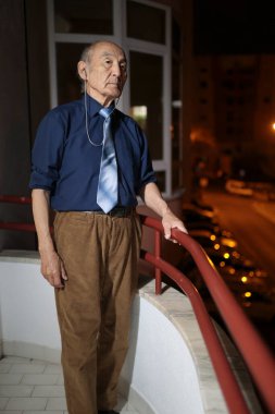 İşitme cihazlı yaşlı profesör geceleri balkonundan şehrin ışıklarının tadını çıkarıyor.