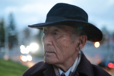 Alacakaranlıkta şehir ortamında müzik dinleyerek şapka ve kulaklık takan son sınıf öğrencisinin portresi.