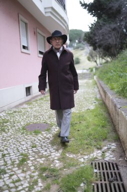 Son sınıf öğrencisi şapkası ve paltosu olan bir adam bir apartmanın yakınındaki kaldırım taşı sokakta yürüyor.