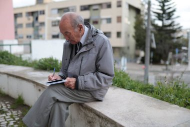 Üst düzey bir adam açık havada bir deftere not alıyor, aktif yaşam tarzını ya da kişisel projelere olan bağlılığını yansıtıyor.