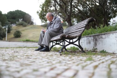 Huzurlu bir park ortamında ahşap bir bankta otururken not alan yaşlı bir adam.