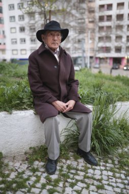 Alçak bir duvarda dinlenen, şapkası ve paltosu olan düşünceli bir son sınıf öğrencisinin portresi.