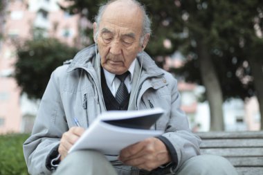 Yaşlı profesör, parkta bir bankta kulaklıkla müzik dinlerken deftere notlar alıyor.