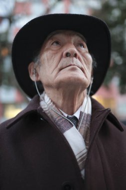 Şapka, kulaklık ve palto giyen şık bir son sınıf öğrencisinin portresi şehir ortamında derin düşüncelere dalmış bir ifadeyle yukarı bakıyor.