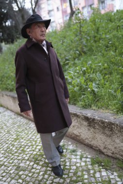 YaşIı bir adam, yerleşim yerinin yakınındaki asfalt bir parkta sakin bir şekilde geziniyor ve kentsel çevrenin sakinliğini kucaklıyor.