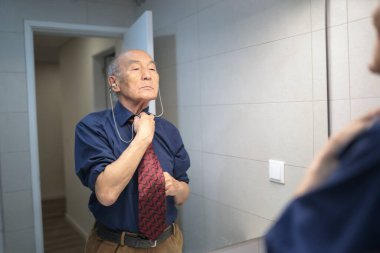 Zarif kıdemli işadamı banyodaki aynanın önünde kravatını düzeltiyor ve iş gününe hazırlanıyor.