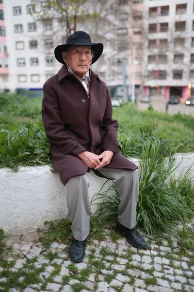 Alçak bir duvarda dinlenen, şapkası ve paltosu olan düşünceli bir son sınıf öğrencisinin portresi.