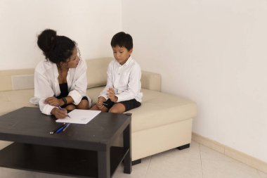 Çocuk psikoloğu terapi seansı sırasında çizdiği resimden bahseden bir çocuğu dinlerken not alıyor.