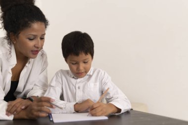 Öğretmeninin okul masasında ona yardım ettiği not defterine odaklanmış genç bir öğrenci.
